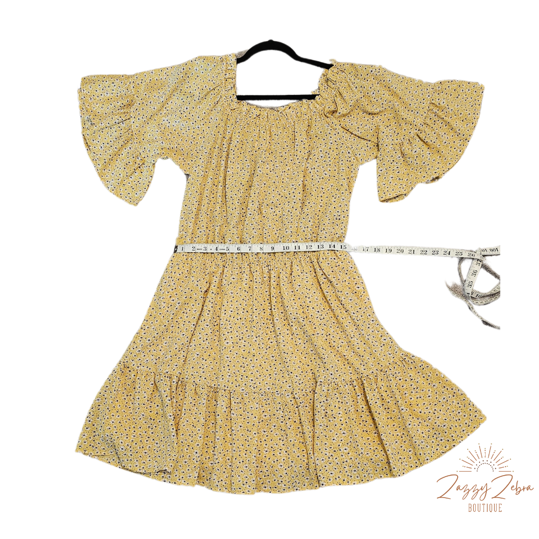 “A Ray Of Sunshine” is a dandelion color mini dress with a floral pattern (white, black, brown, green). This tiered dress features an elastic ruffle rounded neckline, ruffled sleeves, and elastic waistband. It does have a lining and two functional pockets! Imagine yourself in a field of wildflowers making wishes on dandelions. Sizes small through large.