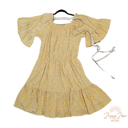 “A Ray Of Sunshine” is a dandelion color mini dress with a floral pattern (white, black, brown, green). This tiered dress features an elastic ruffle rounded neckline, ruffled sleeves, and elastic waistband. It does have a lining and two functional pockets! Imagine yourself in a field of wildflowers making wishes on dandelions. Sizes small through large.