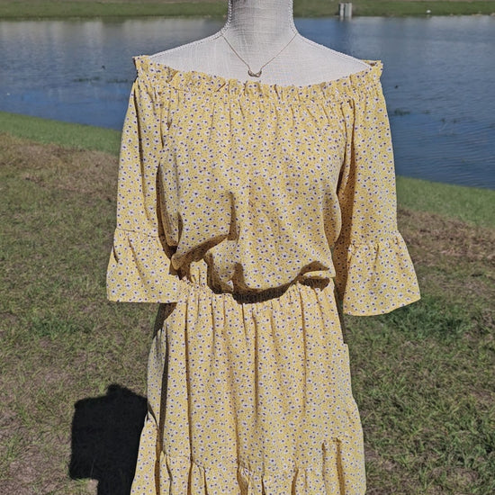 “A Ray Of Sunshine” is a dandelion color mini dress with a floral pattern (white, black, brown, green). This tiered dress features an elastic ruffle rounded neckline, ruffled sleeves, and elastic waistband. It does have a lining and two functional pockets! Imagine yourself in a field of wildflowers making wishes on dandelions. Sizes small through large.