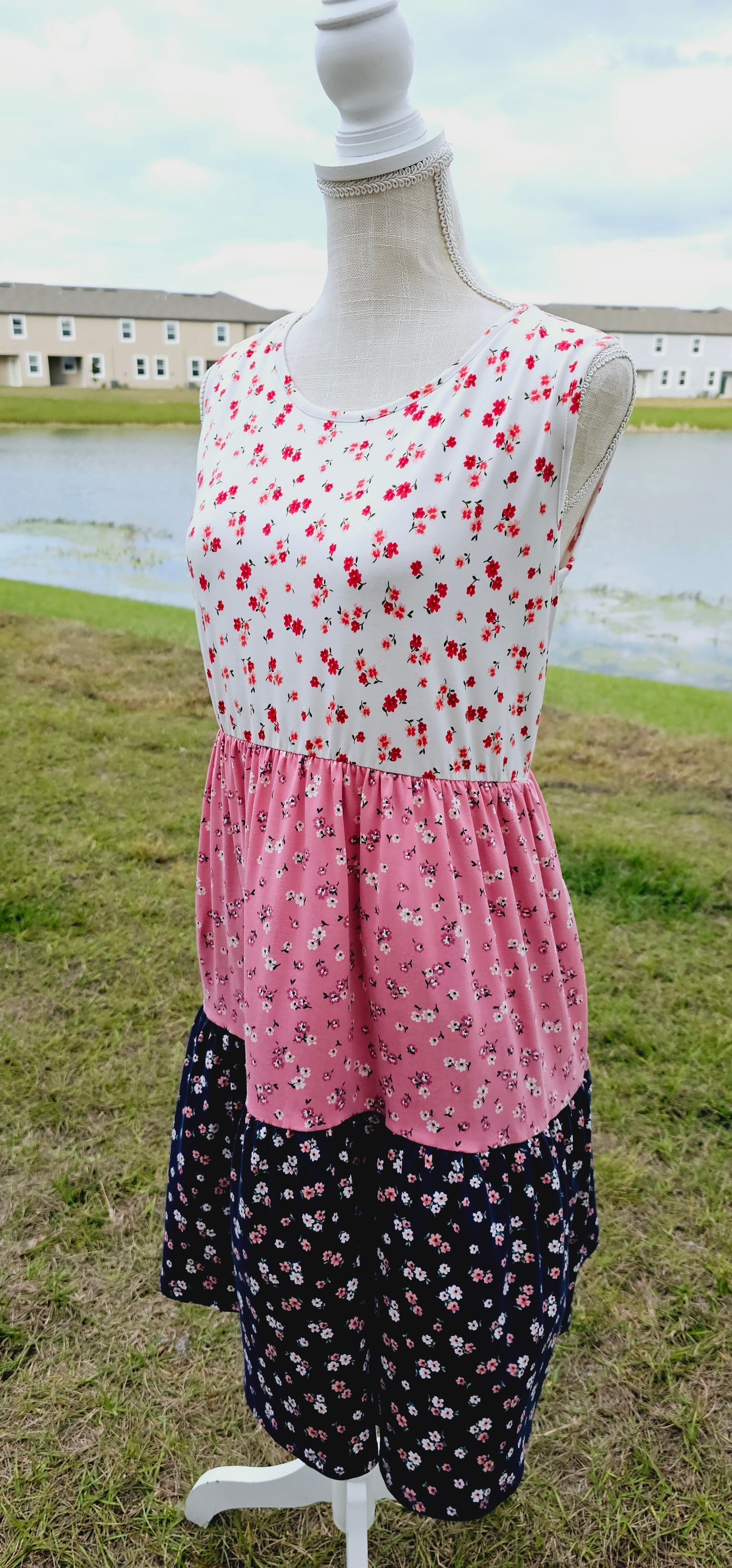 The “Flower Child“ dress is sleeveless, it features a rounded neckline, tiered layers, two functional pockets, and it sits above the knees. It is a buttery soft material. This is unlined, non-sheer, and lightweight. This dress is off white, dusty mauve, and navy blue with red, pink, and dusty mauve flowers. Sizes small through x-large.