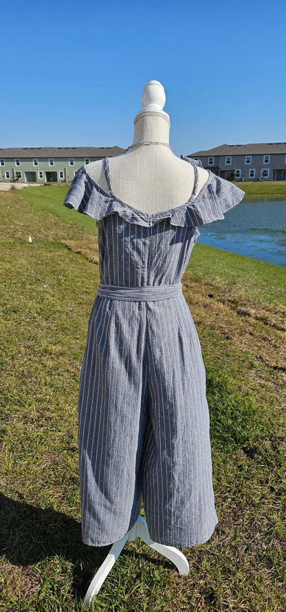 How adorable is the “Cool Breeze” jumpsuit. This jumpsuit features spaghetti straps that are adjustable, ruffled cold shoulder sleeves, ruffles down front in shape of a v, material tie belt for around waist, wide cropped legs, the pants have pockets, zipper and eyelet hook in back, and has gray, white, and black stripes. Just slip it on and you are ready for the day!&nbsp; I hear that a vacation is planned.&nbsp; What a great item to pack in your suitcase. Sizes small through large.