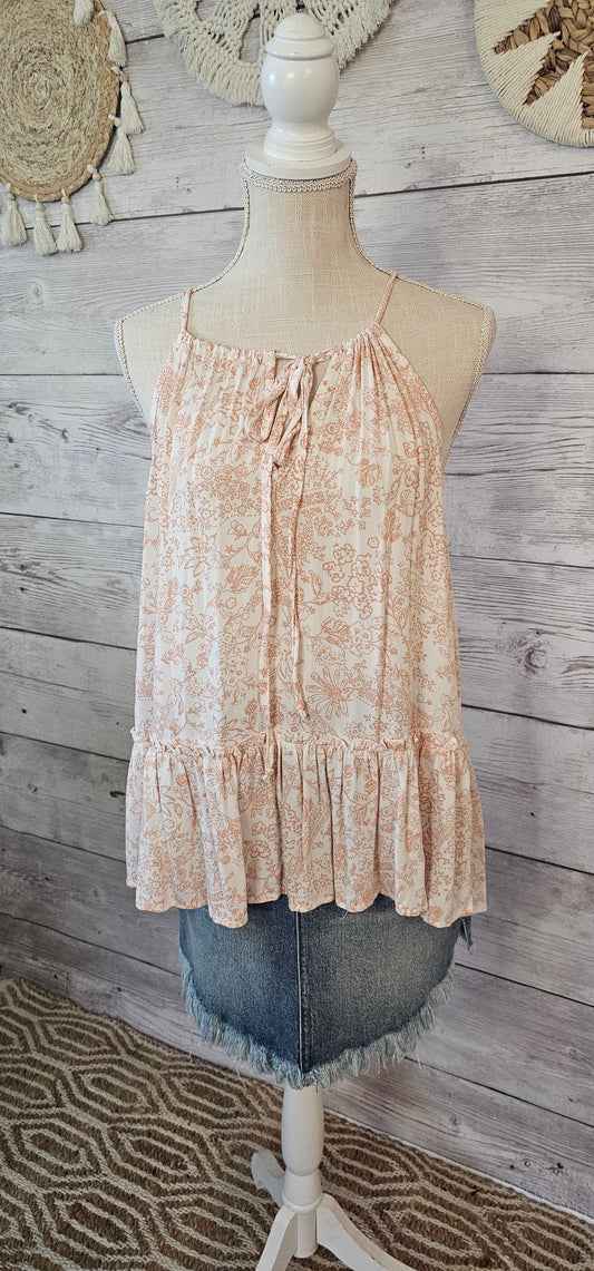 “Peachy Keen” is a peach and off white floral tank top. This top features a self tie closure front with keyhole feature, and high-low ruffled hemline. Sizes small through large.