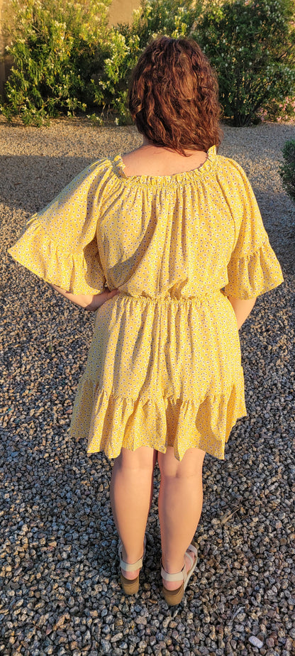 “A Ray Of Sunshine” is a dandelion color mini dress with a floral pattern (white, black, brown, green). This tiered dress features an elastic ruffle rounded neckline, ruffled sleeves, and elastic waistband. It does have a lining and two functional pockets! Imagine yourself in a field of wildflowers making wishes on dandelions. Sizes small through large.