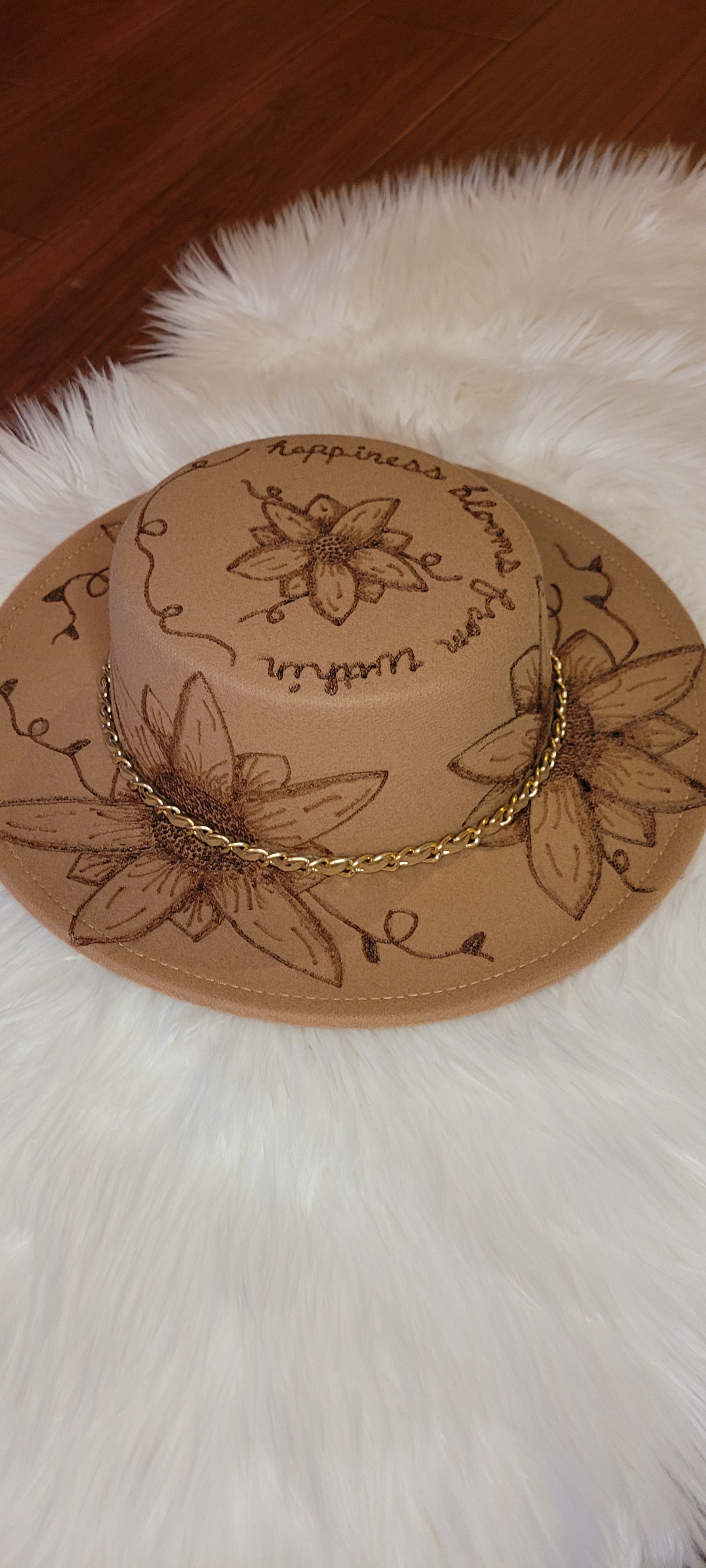 Features flowers, leaves & "Happiness Blooms From Within" engraving Chain with faux leather Felt hat Flat brim 100% polyester Ribbon drawstring for hat size adjustment Head Circumference: 24" Crown Height: 3.5" Brim Length: 13.5" Brim Width: 12.75" Branded & numbered inside crown Custom engraved by Kayla