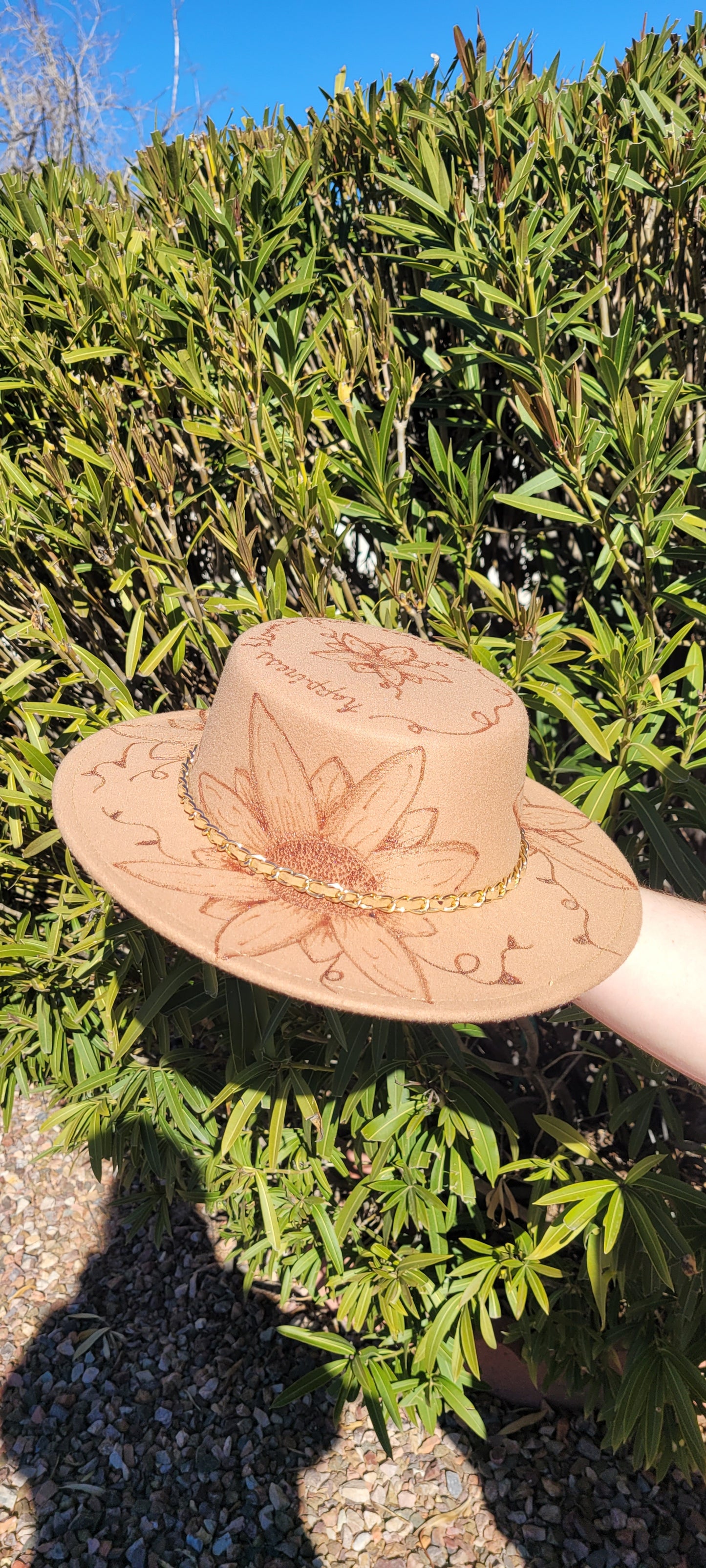 Features flowers, leaves & "Happiness Blooms From Within" engraving Chain with faux leather Felt hat Flat brim 100% polyester Ribbon drawstring for hat size adjustment Head Circumference: 24" Crown Height: 3.5" Brim Length: 13.5" Brim Width: 12.75" Branded & numbered inside crown Custom engraved by Kayla