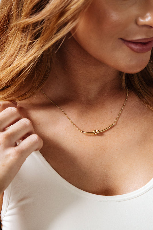 This Love Knot Bar Necklace is the perfect gift for a special someone. Crafted with 18k-gold plated stainless steel and featuring a stylish and modern link chain with a fixed bar pendant with a knotted detail, it will add a touch of sophistication and style to any outfit.  18K gold plated stainless steel means you can wear this piece to the beach, the pool, or even working out without worrying over tarnishing, green marks, or skin irritation