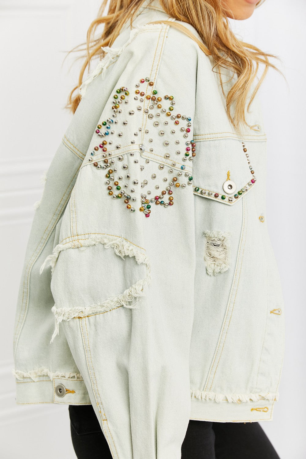 You will definitely turn head with this timeless denim jacket. This relaxed fit jacket features button front closures, distressed detailing and colorful pearl beaded details along the sleeves and front pockets. Pair with a dress or pants for an elevated casual look.